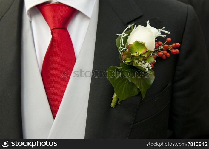 White rose in the buttonhole of the tail-coat of a groom, complementing the red necktie