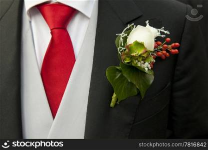 White rose in the buttonhole of the tail-coat of a groom, complementing the red necktie