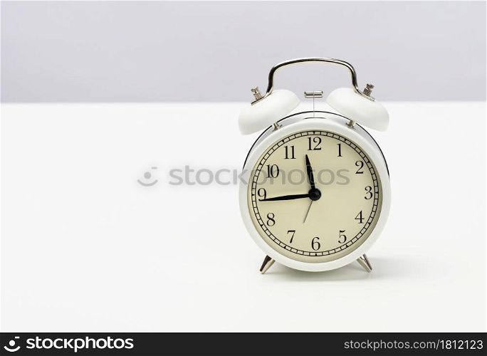 white round alarm clock stands on the table, the time is fifteen minutes to twelve