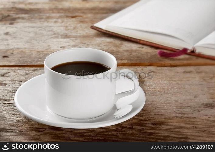 White round cup with black coffee on a wooden table with a book