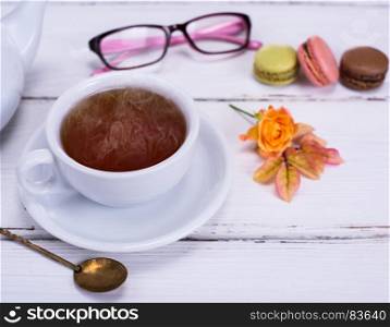 white round cup with black tea on a white wooden background, behind a cake and glasses