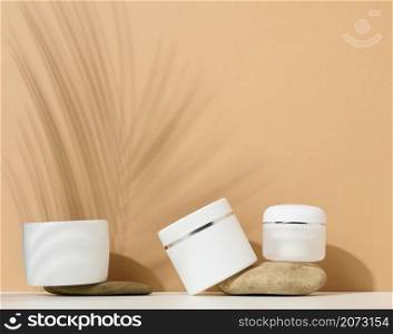 white round plastic jar for cosmetic products on a brown background. Palm leaf shadow. Blank for branding products, mock up