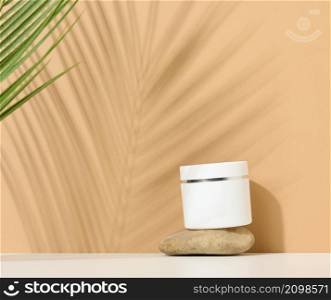 white round plastic jar for cosmetic products on a brown background. Palm leaf shadow. Blank for branding products, mock up