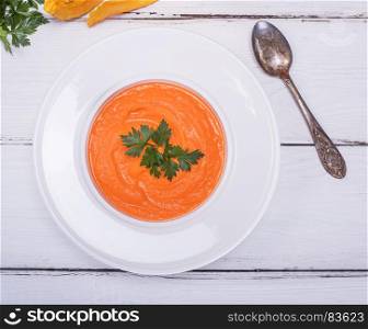 white round plate with cream of pumpkin soup on white wooden background, top view