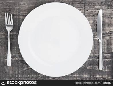 White round plate with fork and knife on wooden board background