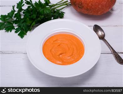 white round plate with pumpkin soup on a white wooden background, top view