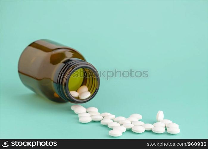 White round tablets scattered in front of glass bottle of pills. White round tablets scattered near glass bottle of pills