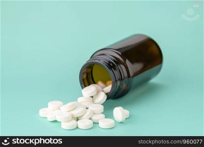 White round tablets scattered near glass bottle of pills. White round tablets scattered in front of glass bottle of pills