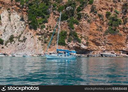 White Sailboat Anchored on Serene Sea, orange Majestic Rock in background: Sardinia Coastline- Italy