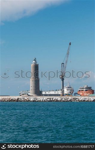 White Sailboat in the Sea and Crane at Work in Boatyard near Lighthouse