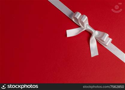 White satin ribbon bow on red paper background. White bow on red