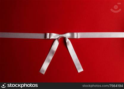 White satin ribbon bow on red paper background. White bow on red