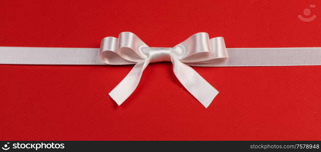 White satin ribbon bow on red paper background. White bow on red