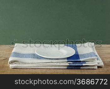 White saucer and dishcloth on old wooden table over green background