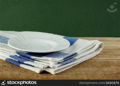 White saucer and dishcloth on old wooden table over green background