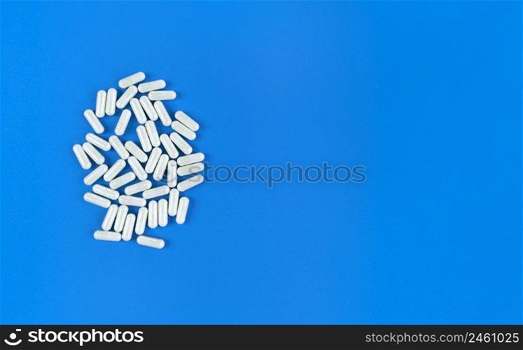 White scattered pills capsules on a blue backdrop with copy space.. White scattered pills capsules on blue backdrop with copy space.