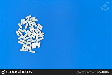 White scattered pills capsules on a blue backdrop with copy space.. White scattered pills capsules on blue backdrop with copy space.
