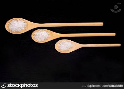 White sea bath salt in wooden spoons on a dark polished table
