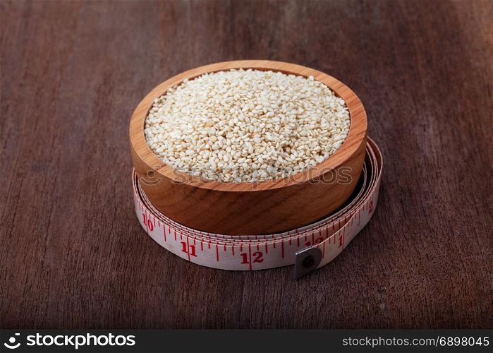 white sesame seeds in wooden bowl with measuring tape on wood background
