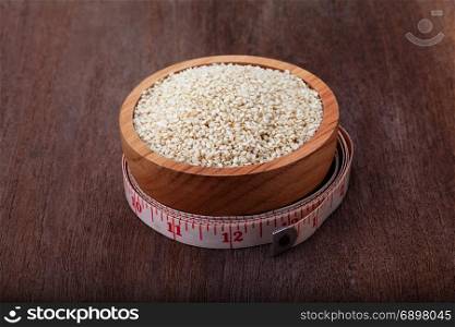white sesame seeds in wooden bowl with measuring tape on wood background