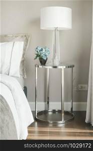 White shade reading lamp and blue rose on glass top stainless steel frame bedside table next to bed