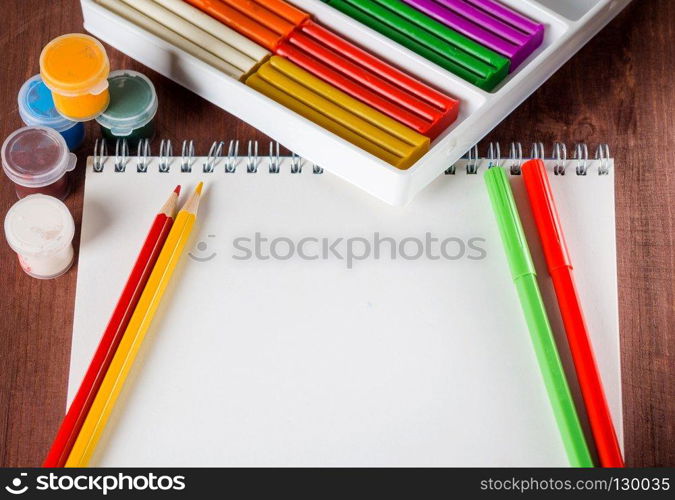 White sheet of paper pencils and colored paint on the wooden background