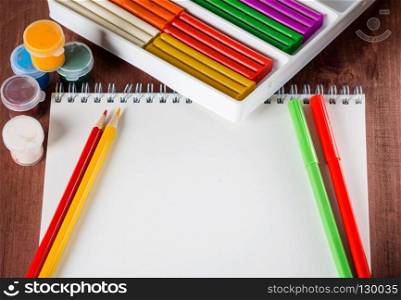 White sheet of paper pencils and colored paint on the wooden background
