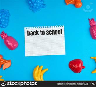 white sheet torn out of notepad on a blue background in the midst of childish toys, inscription back to school