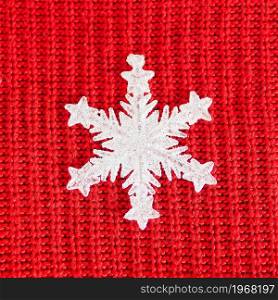 white shiny figurine of a snowflake on a red knitted background.