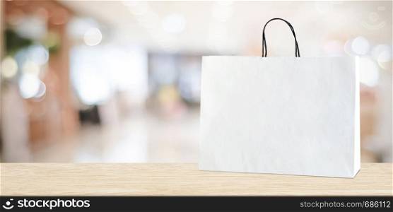 White shopping bag on wooden table over blurred store background, business, template, product display montage background