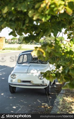 White small vintage car on the street. No people. Asphalt village road in Italy. Travel concept with car.