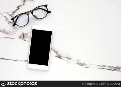 White smart phone with blank screen and eyeglasses on white marble table background for mock up, template, technology and lifestyle concept