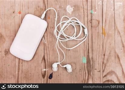 White smart phone with earphones on grunge wooden desk.