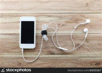 White smartphone on brown wood background and a headset is Device connected,concept of music and technology.