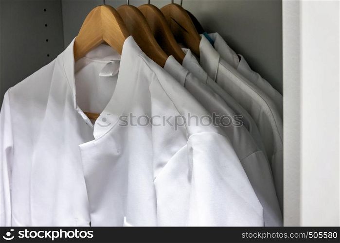 White smocks on wooden hangers hang in the cupboard of a laboratory