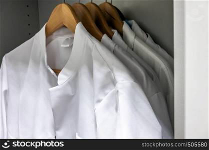 White smocks on wooden hangers hang in the cupboard of a laboratory