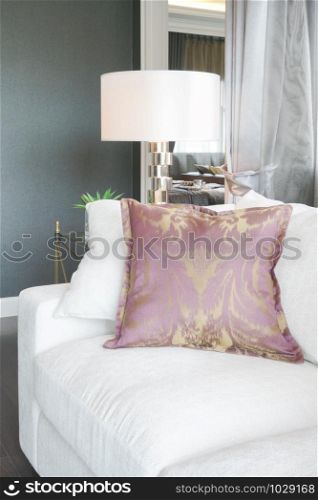 White sofa with purple pillow, reading lamp in background