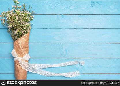 White spring flowers bouquet with lace ribbon, tied bow, wrapped in vintage paper, on an empty blue desktop. Flat lay. Copy space. Women day frame.