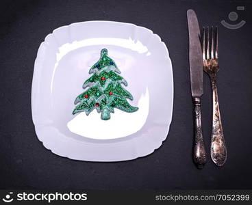 white square plate with Christmas decorations near iron cutlery on black background, top view