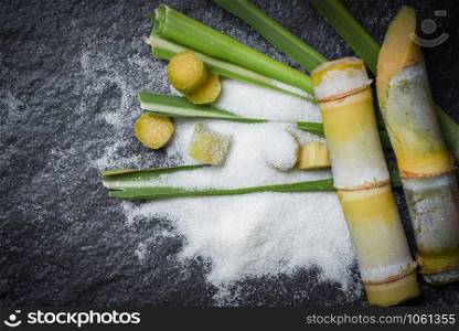 White sugar and and green of leaf cut sugar cane piece on dark background