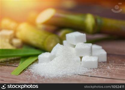 White sugar cubes and sugar cane on wooden table and sunlight nature background