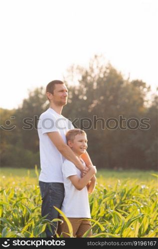 white t-shirt, advertising space, children&rsquo;s clothing, look at dad, dad hugs, holding hands, walk with dad, stand on the street, corn field, walk in the field, family walk, sunset. Cute boy hugs his dad at sunset. White T-shirts