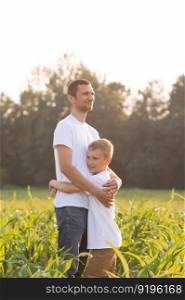 white t-shirt, advertising space, children&rsquo;s clothing, look at dad, dad hugs, holding hands, walk with dad, stand on the street, corn field, walk in the field, family walk, sunset. Cute boy hugs his dad at sunset. White T-shirts