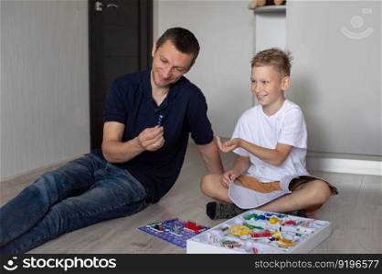 white t-shirt, electrical designer, lots of details, boy and man, dad and son, sit on the floor, play a game, read the instructions. A cute boy in a white T-shirt collects an electrical designer with his dad in the room