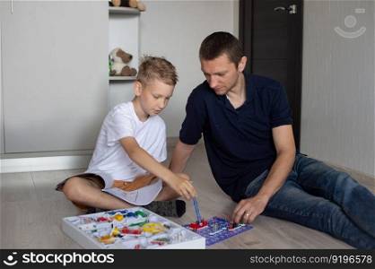 white t-shirt, electrical designer, lots of details, boy and man, dad and son, sit on the floor, play a game, read the instructions. A cute boy in a white T-shirt collects an electrical designer with his dad in the room