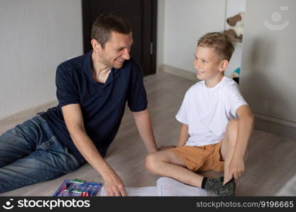 white t-shirt, electrical designer, lots of details, boy and man, dad and son, sit on the floor, play a game, read the instructions. A cute boy in a white T-shirt collects an electrical designer with his dad in the room