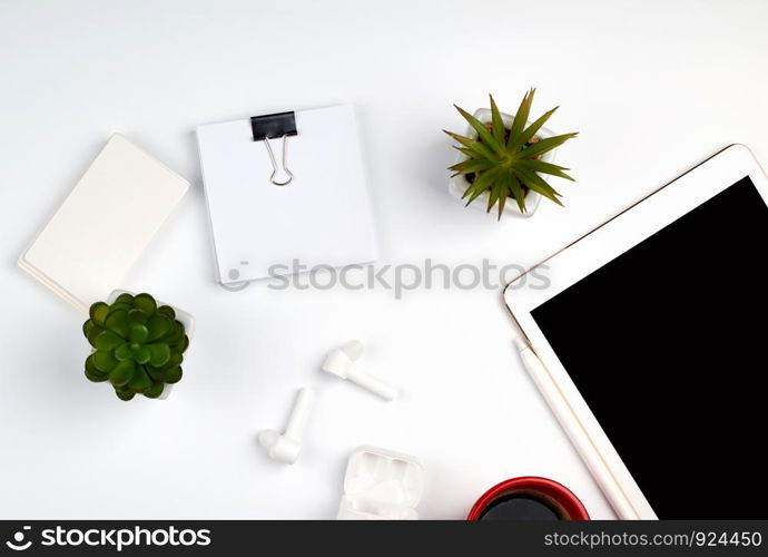 white table with electronic tablet, blank business cards, cup of coffee and wireless headphones, workplace of a freelancer or designer, top view, copy space