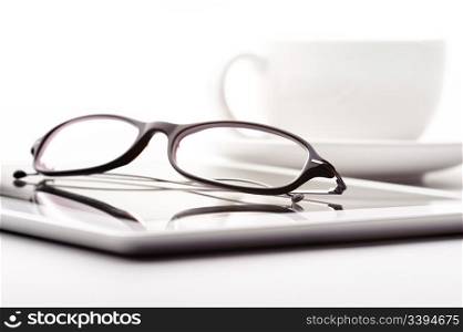 White tablet, coffee cup and glasses on a white table. Still life with white tablet, coffee cup and glasses on a white table