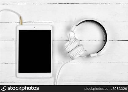 White tablet computer and the white headphones on white boards. White tablet computer and the white headphones