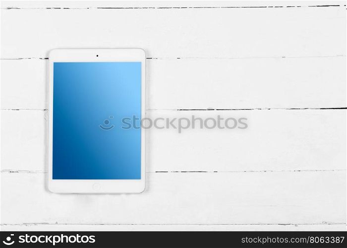 White tablet with blue screen on wooden white table. White tablet with blue screen